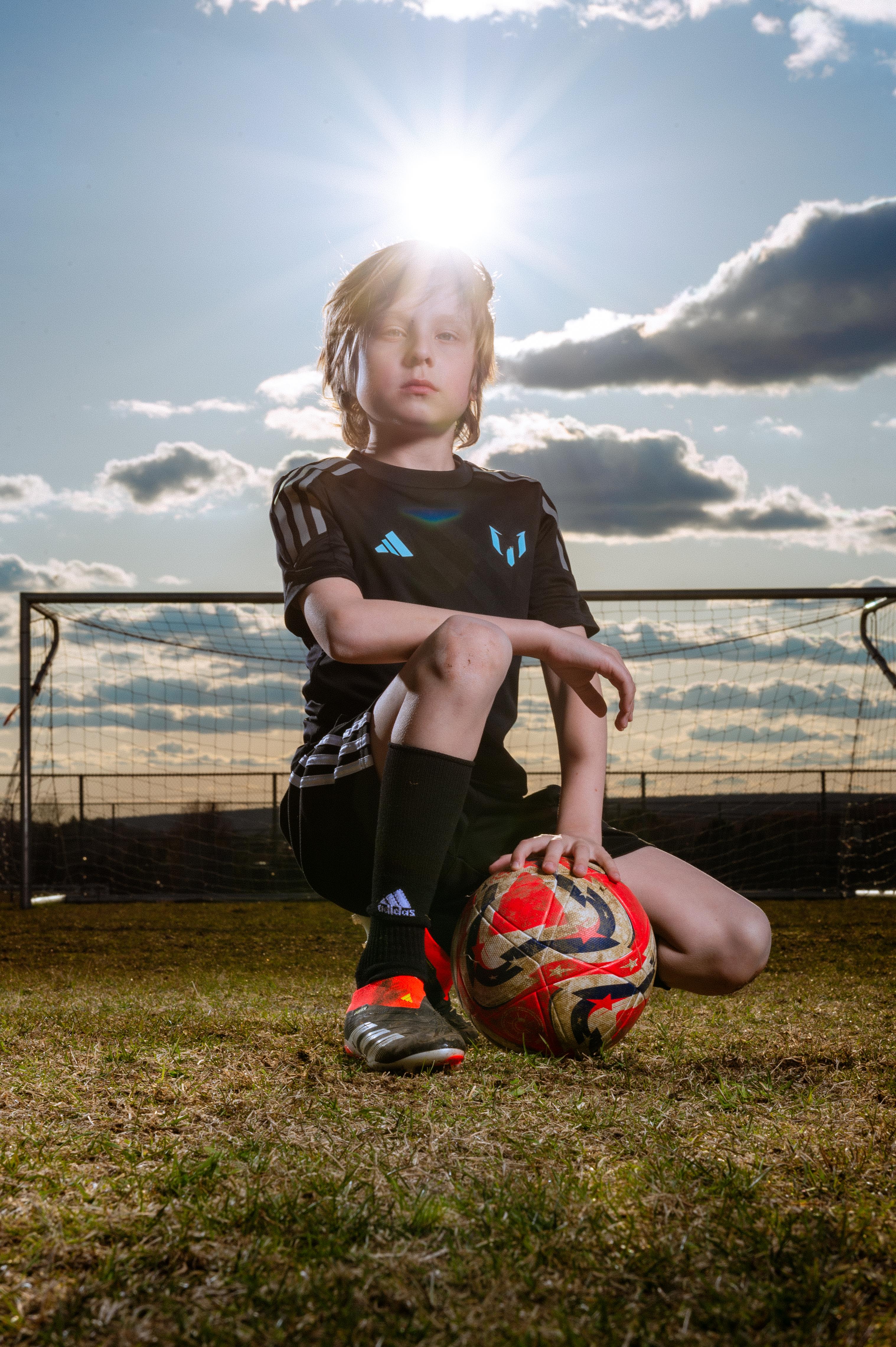 soccer player posing with a ball at sunset